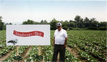 Cecil Henderson standing in a field beside a Henderson's Best sign